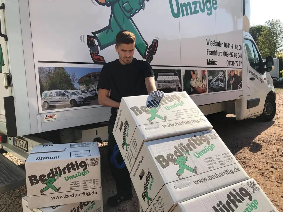 Mitarbeiter von Bedürftig Umzüge mit Umzugskartons vor einem firmeneigenen Umzugsfahrzeug